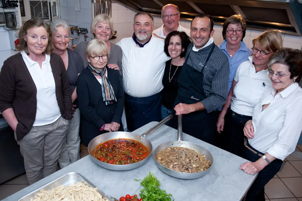 Un gruppo di ospiti in cucina con lo chef davanti a due padelle